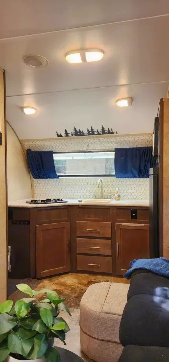 Cozy RV rental kitchen with hexagonal tile backsplash, stovetop, sink, and wooden cabinets. Pine tree decor accents the space.. Winnebago MicroMini 2306 BHS 2020