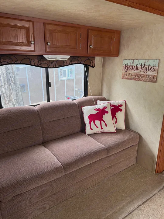 Inside this RV rental, a brown sofa with red moose pillows sits below wood cabinets. A 'Beach Rules' sign adds decor.. Holiday Rambler Campmaster 2011