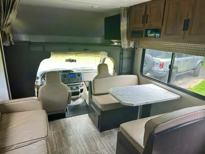 Inside a well-appointed RV rental, featuring the driver's cab, a dinette with table, and a living room sofa. Perfect for travel.. Forest River Sunseeker LE 2019