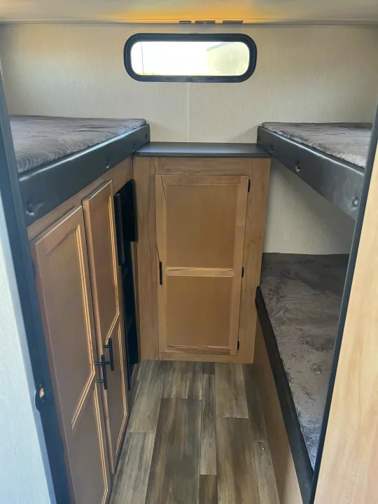 RV rental bunk beds: a cozy interior with storage cabinets, a horizontal window, and wood-look flooring for your travels.. Forest River 29TE 2023