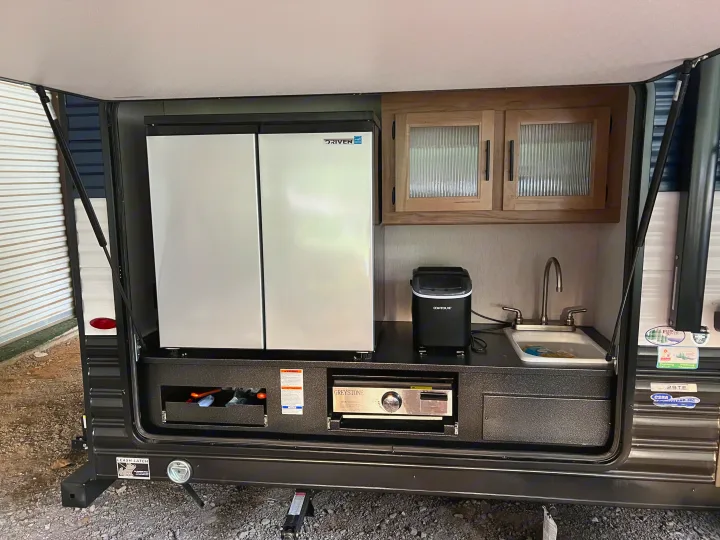 An RV rental's outdoor kitchen, equipped with a refrigerator, sink, ice maker, and built-in griddle, perfect for camp cooking.. Forest River 29TE 2023