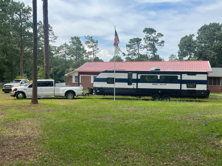 White dually truck towing a black & white Grey Wolf travel trailer RV rental on a grassy lot with a house & trees.. Forest River 29TE 2023