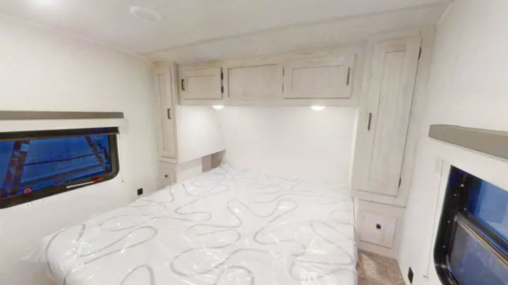 Modern RV rental bedroom interior features a light-toned bed, overhead and side cabinets, and windows, ready for your adventure.. East to West Della Terra 2023