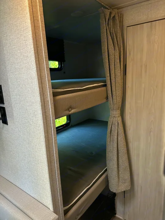 Cozy RV rental bunk beds with privacy curtains. This RV interior offers comfortable sleeping for travelers.. East to West Della Terra 2023