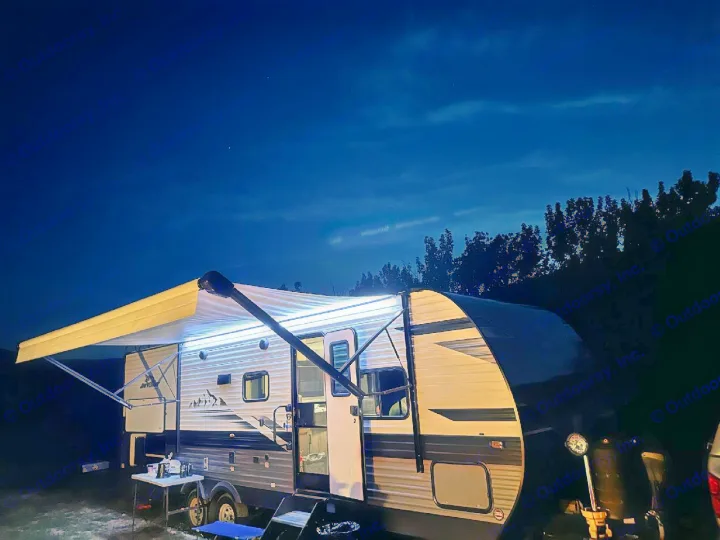 Enjoying the night in an RV rental. Its bright awning lights illuminate the cozy campsite setup, perfect for outdoor relaxation.. Jayco Jay Flight 2023