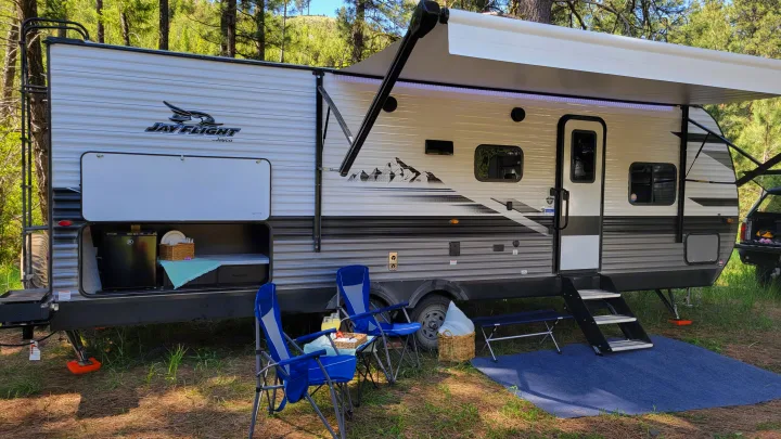 This RV rental shows a travel trailer with an extended awning, outdoor kitchen, chairs, and mat for comfy camping.. Jayco Jay Flight 2023