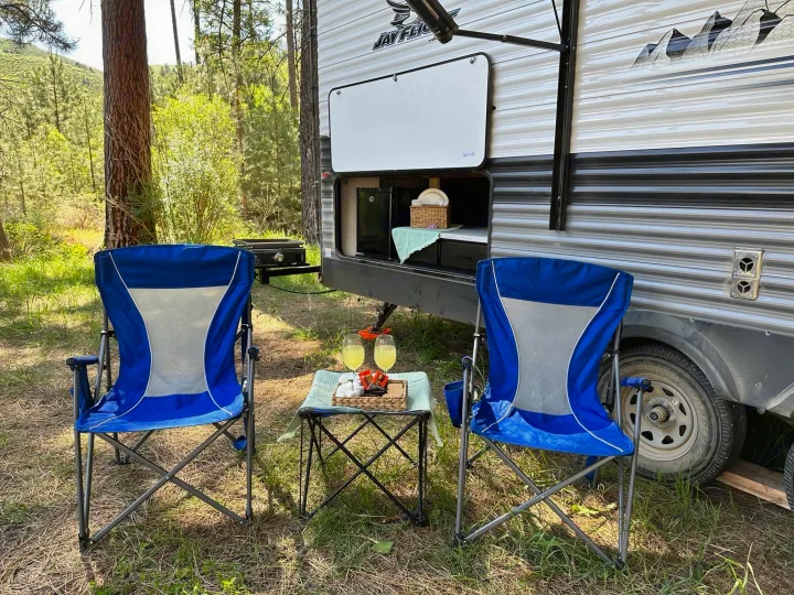 RV rental campsite setup: outdoor kitchen, blue chairs, and s'mores on table in a wooded area, perfect for glamping.. Jayco Jay Flight 2023