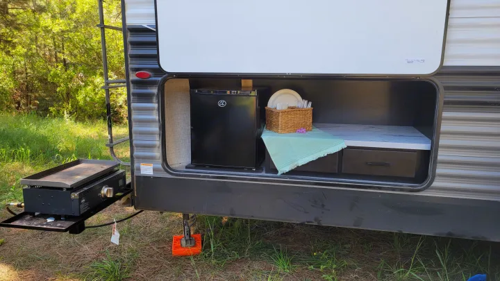 RV rental outdoor kitchen setup: A side compartment open to reveal a mini-fridge, dinnerware, and a griddle ready for camping.. Jayco Jay Flight 2023