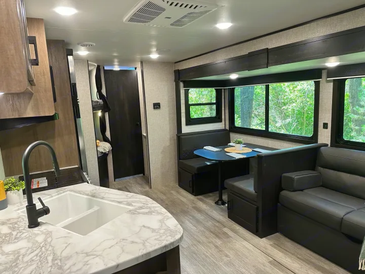 Bright rv rental interior: kitchen with sink, dining booth, and comfy couch. Large windows offer scenic views.. Jayco Jay Flight 2023