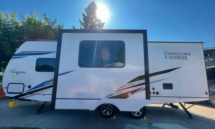 White Coachmen Freedom Express travel trailer, great for rv rental, is parked with its slide-out extended under sunny sky.. Coachmen 257BHS 2022