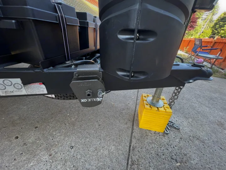 An RV rental travel trailer tongue, showing its Blue Ox hitch, battery, propane, and jack on yellow leveling blocks.. Coachmen 257BHS 2022