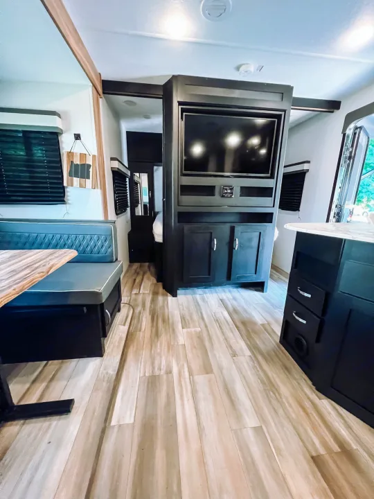 Modern RV rental interior with light wood flooring, dark cabinetry, and a cozy dining booth near an entertainment center.. Coachmen 257BHS 2022