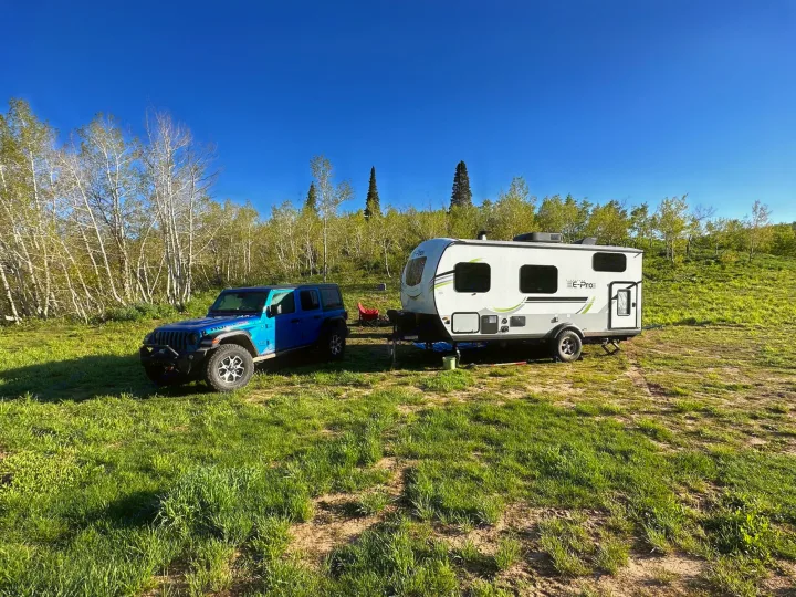 Blue Jeep and RV rental parked off-road in a grassy landscape with trees under a clear blue sky.. Forest River Flagstaff E-Pro 2023