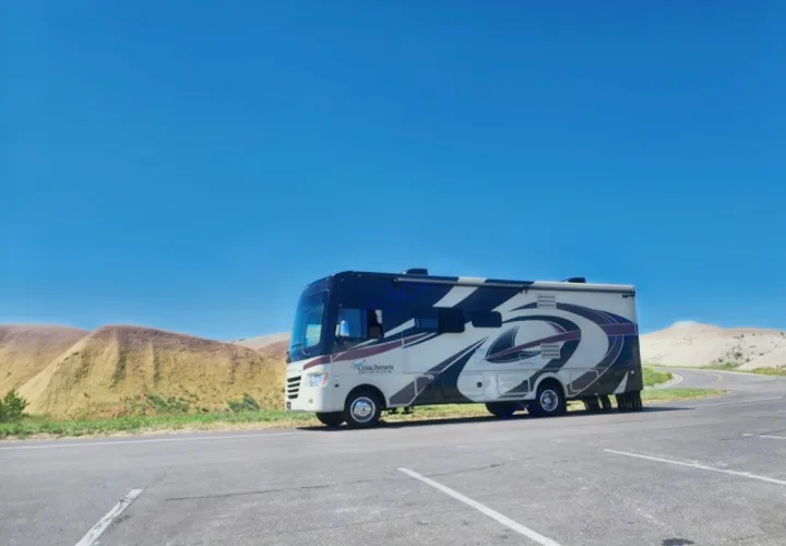 Cream and blue Coachmen Mirada RV rental parked on a paved road, set against arid, rolling hills under a bright blue sky.. Coachman Mirada 2018