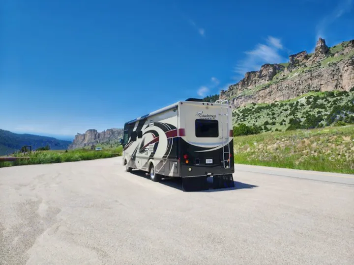 RV rental parked at a scenic mountain overlook, showcasing majestic cliffs, distant peaks, and a clear blue sky.. Coachman Mirada 2018