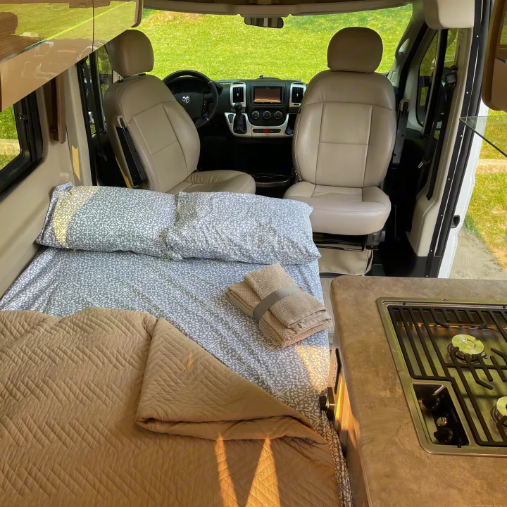 This RV rental interior features a comfortable bed with soft bedding, a compact kitchen with a stovetop, and the front driving cabin.. Thor Motor Coach Scope 2022