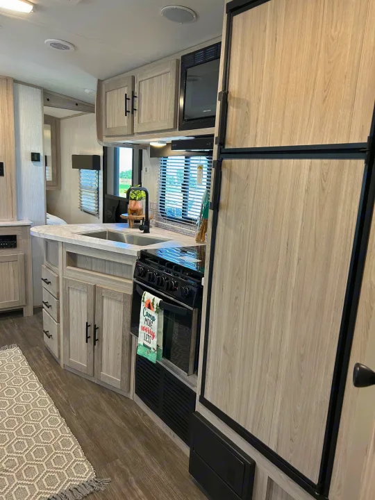 This modern RV rental kitchen has light wood-look cabinets, a sink, stove, microwave, and integrated panel fridge.. Cruiser RV Shadow Cruiser 2022