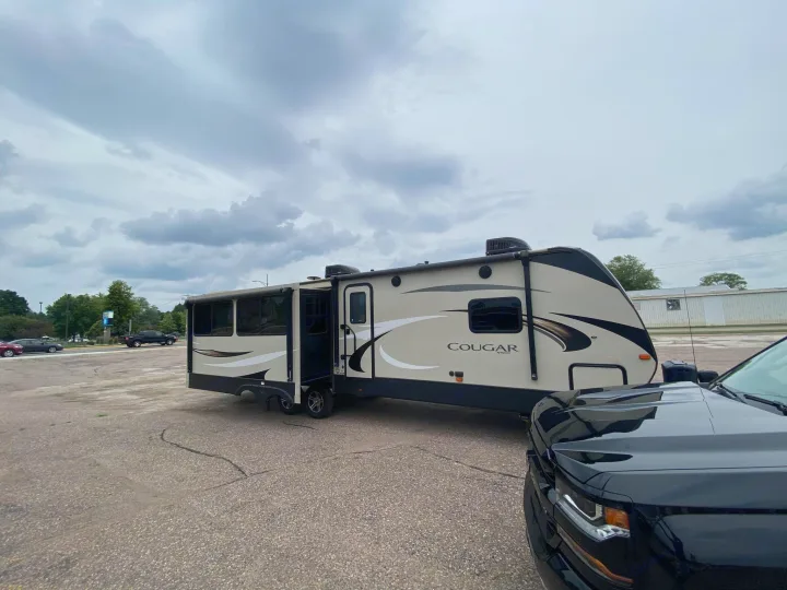 Cougar travel trailer with slide-outs, hitched to a black truck in a lot, ready for your next RV rental adventure.. Keystone RV Cougar 2019