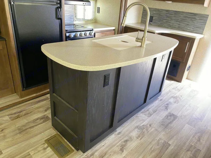 Modern RV rental kitchen with dark wood island, light countertop, sink, and stainless faucet. Black fridge & stove.. Keystone RV Cougar 2019