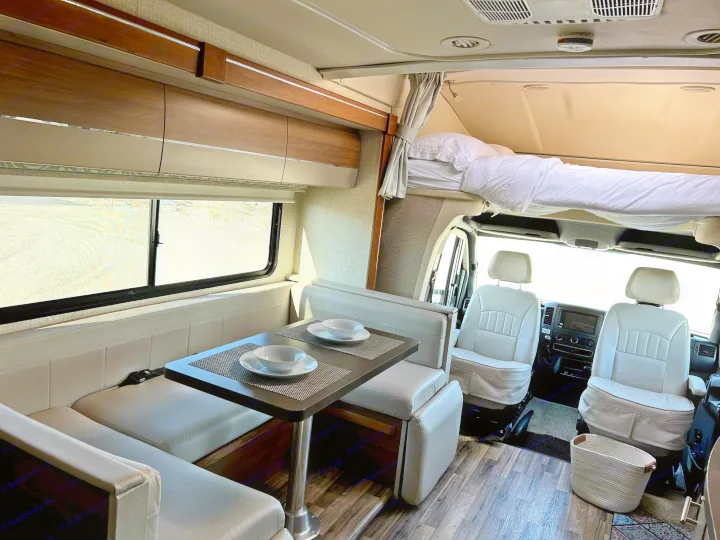Bright RV rental interior: A full view of the dinette, comfortable overhead bunk, and front driver's cab seating. Ready for travel!. Winnebago View 2017