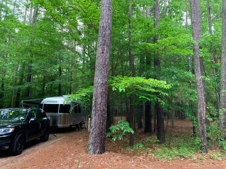 RV rental adventure begins! Black SUV tows an Airstream travel trailer in a serene forest campsite with lush green trees.. Airstream Caraval 2021