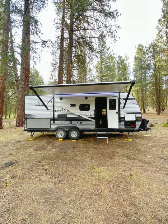 Spacious travel trailer RV rental perfectly set up in a serene pine forest campsite, ready for adventure.. Jayco Jay Flight 2023