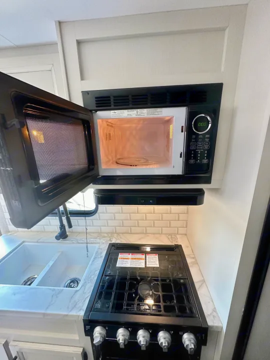 RV rental kitchen: An open overhead microwave, double sink, and gas range are ready for your next adventure.. Jayco Jay Flight 2023