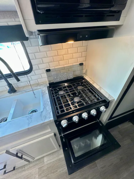 RV rental kitchen: This compact interior features a black gas range, open oven, and double sink with subway tile backsplash.. Jayco Jay Flight 2023