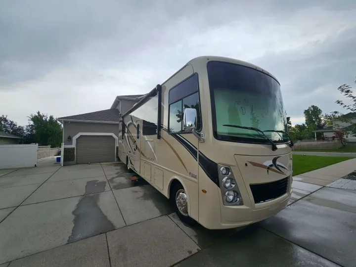 Spacious RV rental on a driveway with extended awning. Ready for family adventures under overcast skies.. Thor Freedom Traveler 2020
