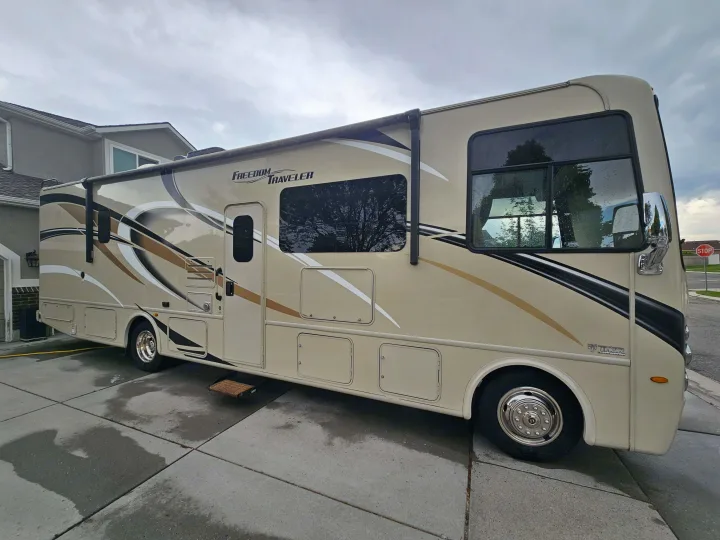 Spacious beige Thor Freedom Traveler RV on a wet driveway, ideal for an RV rental and exploring new horizons.. Thor Freedom Traveler 2020