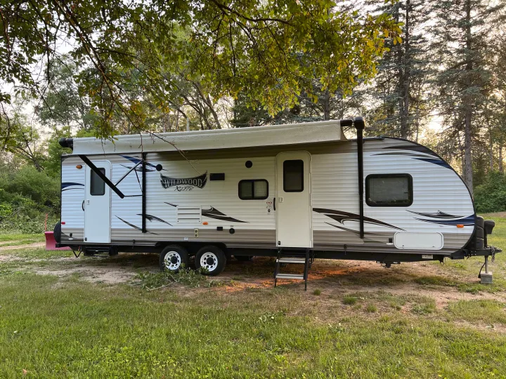 This white RV rental, a Wildwood X-Lite travel trailer, is set up at a wooded campsite.. Forest River Wildwood X-Lite 2015