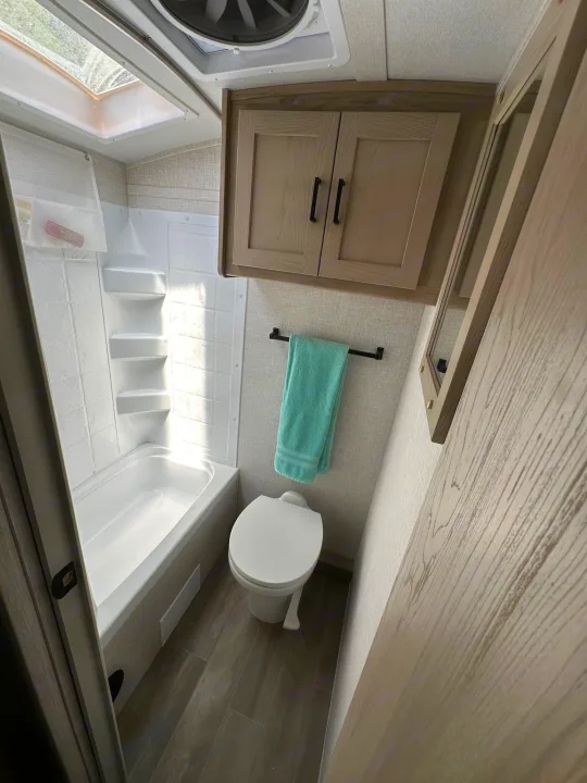 This clean RV rental bathroom offers a tub/shower, toilet, cabinet storage, and skylight, perfect for travel comfort.. Forest River Flagstaff E-Pro 2023