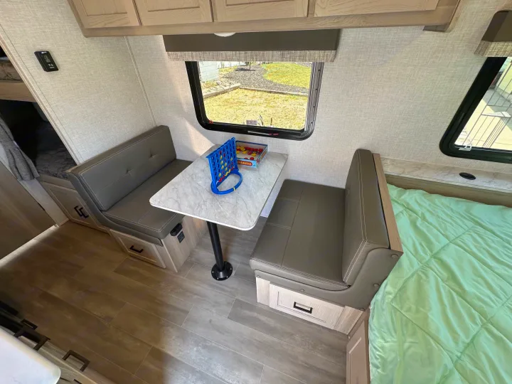 Inside this rv rental: a compact dinette with gray benches, central table (Connect Four), and window view. Includes storage drawers, bed & bunks.. Forest River Flagstaff E-Pro 2023