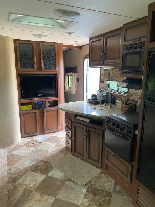 Modern RV rental interior showcasing a functional kitchen with dark wood cabinets, oven, microwave, and entertainment center.. Crossroads RV Zinger 2014