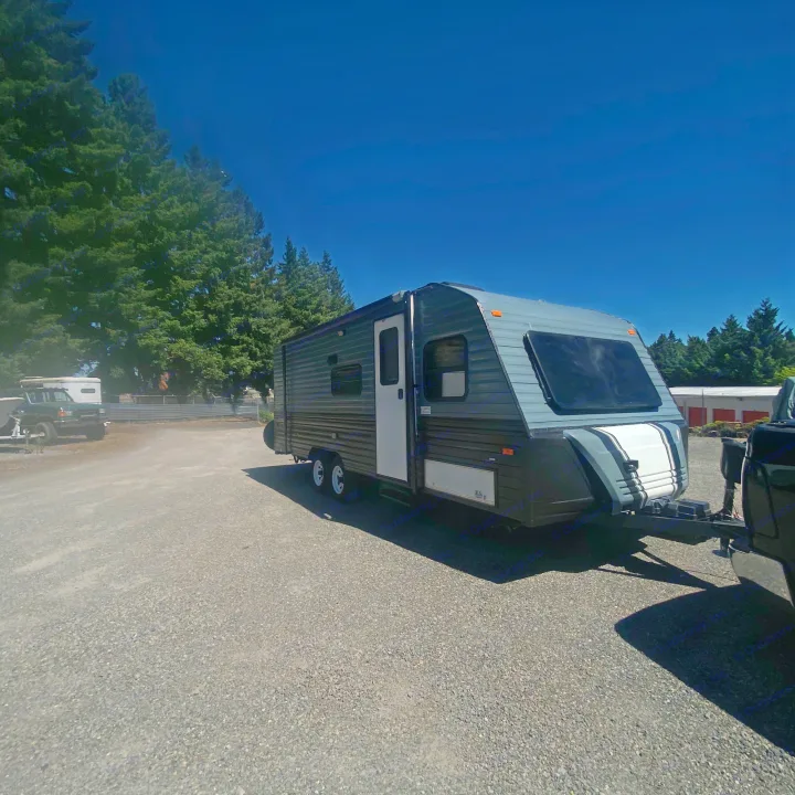 Modern gray travel trailer RV rental, ready for adventure on a sunny gravel lot with trees. Clear blue sky overhead.. Fleetwood Prowler 1996