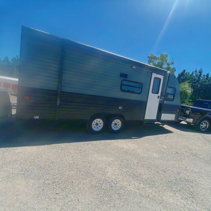 Side view of a dark gray RV rental, a travel trailer, hitched to a pickup truck on a gravel lot under a clear sky.. Fleetwood Prowler 1996