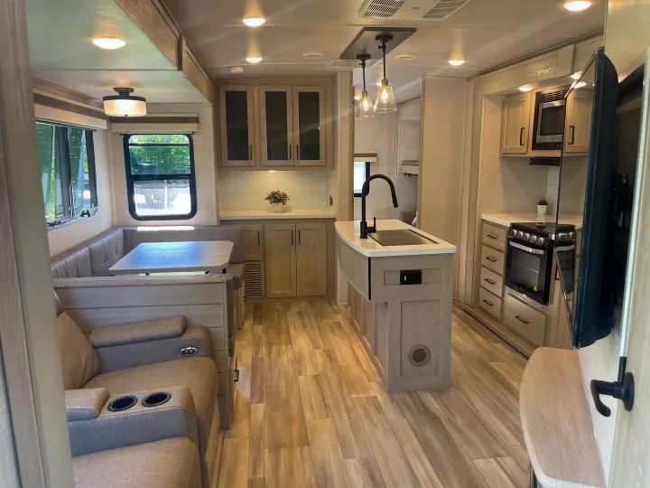 Spacious, modern RV rental interior featuring a kitchen island, dinette, recliners, and light wood finishes.. Forest River Rockwood Signature 2023