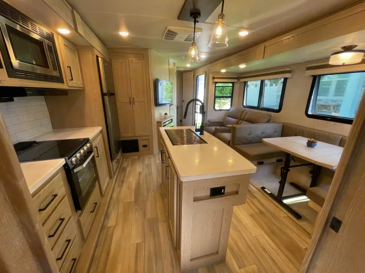 Modern RV rental interior with a fully equipped kitchen, central island, and comfy sofa/dinette for travel comfort.. Forest River Rockwood Signature 2023