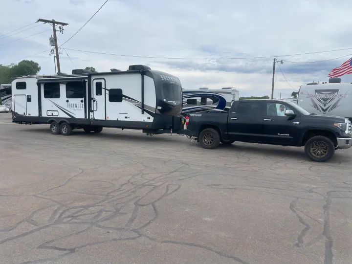 A black truck tows a large white Rockwood travel trailer. This modern RV rental is ready for adventure in a busy lot.. Forest River Rockwood Signature 2023