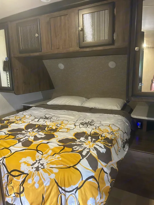 Cozy RV rental bedroom featuring a bed with vibrant yellow and brown floral duvet, built-in storage, and side tables.. Heartland RVs Mallard 2020