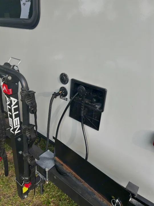 Side view of an RV rental showing an Allen bike rack, city water connection, and an open outdoor shower.. Heartland RVs Mallard 2020
