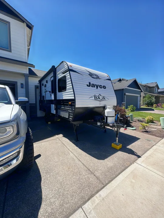 A white Jayco travel trailer, an RV rental, parked in a sunny driveway next to a white pickup truck. Clear blue sky.. Jayco Jay Flight SLX Baja Edition 2022