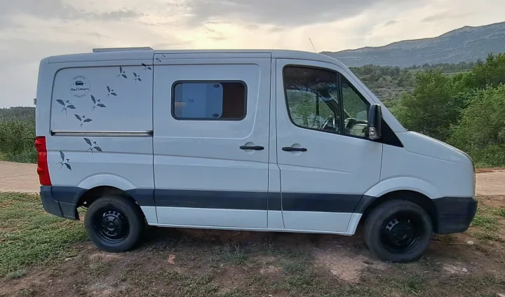 The light-colored Mad Campers van, adorned with bird decals, is ready for an outdoor RV rental adventure.. volkswagen crafter 2014