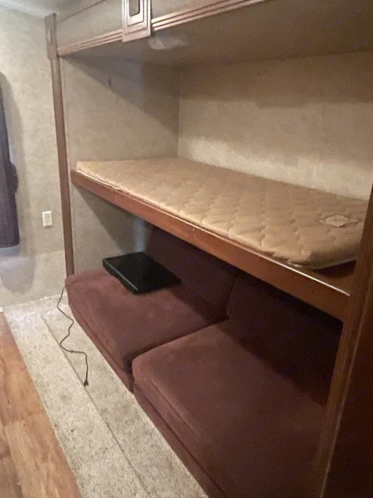 RV rental interior: top bunk bed with mattress, lower sofa seating with device, ideal for compact travel.. Keystone RV Bullet Premier Ultra 2014