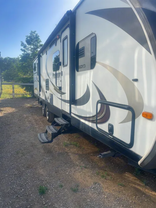 Side view of an RV rental with steps down on a gravel lot under sunny skies.. Keystone RV Bullet Premier Ultra 2014