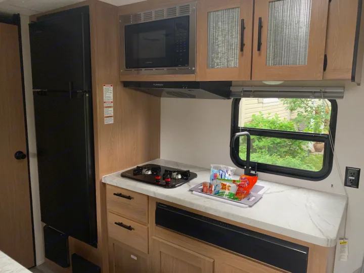 An RV rental's well-equipped kitchen space, showing a black refrigerator, microwave, and stovetop on a marble counter.. Avenger LT 2022