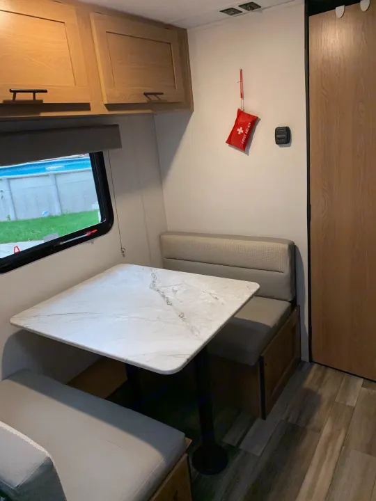 This RV rental interior features a bright dinette with a marble-look table, light wood cabinets, and a scenic window view.. Avenger LT 2022