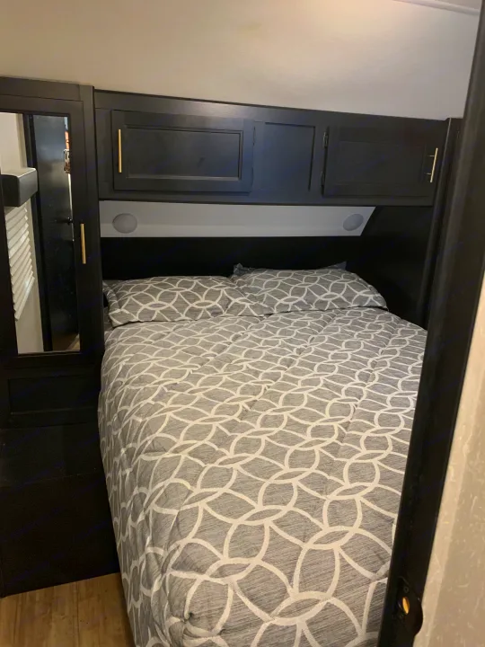 This inviting RV rental bedroom features a comfy bed with modern gray bedding, dark cabinets, and a mirrored wardrobe.. Forest River Cherokee Grey Wolf Black Label 2021