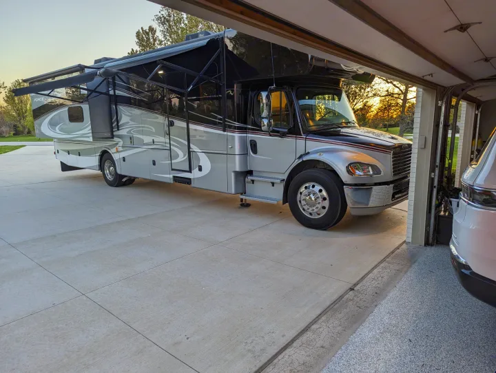 This spacious grey RV motorhome rental, with extended awnings & slides, is parked on a driveway at sunset.. Dynamax Force 2015