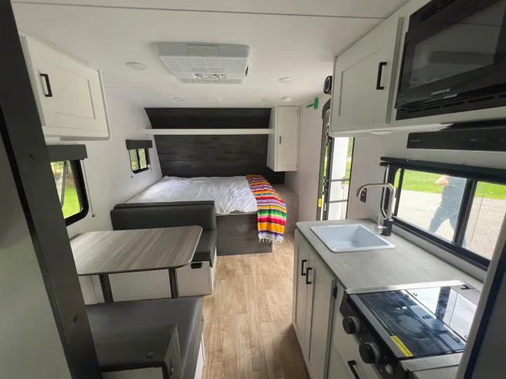 Bright rv rental interior featuring a compact kitchen with stove and sink, a dining area, and a comfortable bed.. Keystone RV Hideout 2023